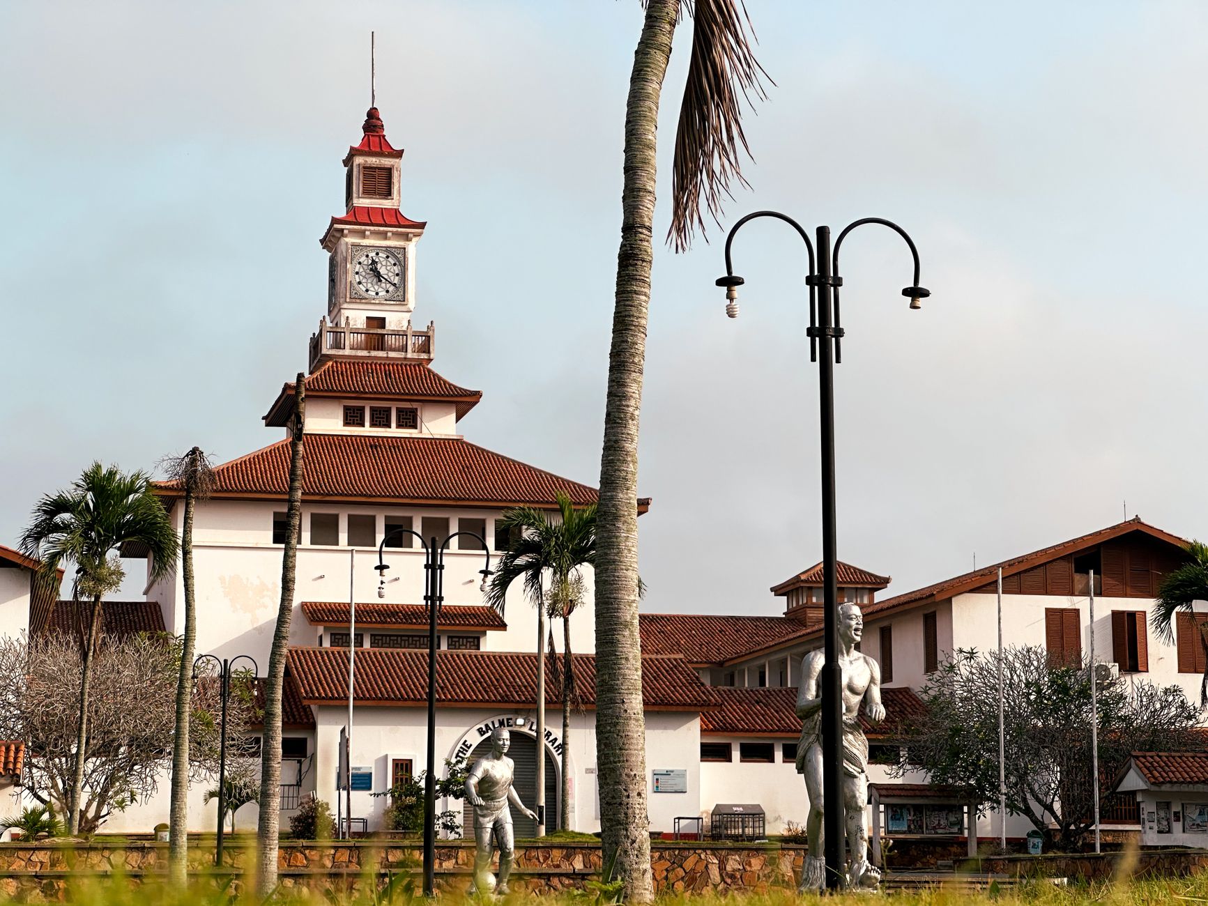 Pemandangan eksterior Perpustakaan Balme di Universitas Ghana dengan pohon palem dan langit yang cerah.