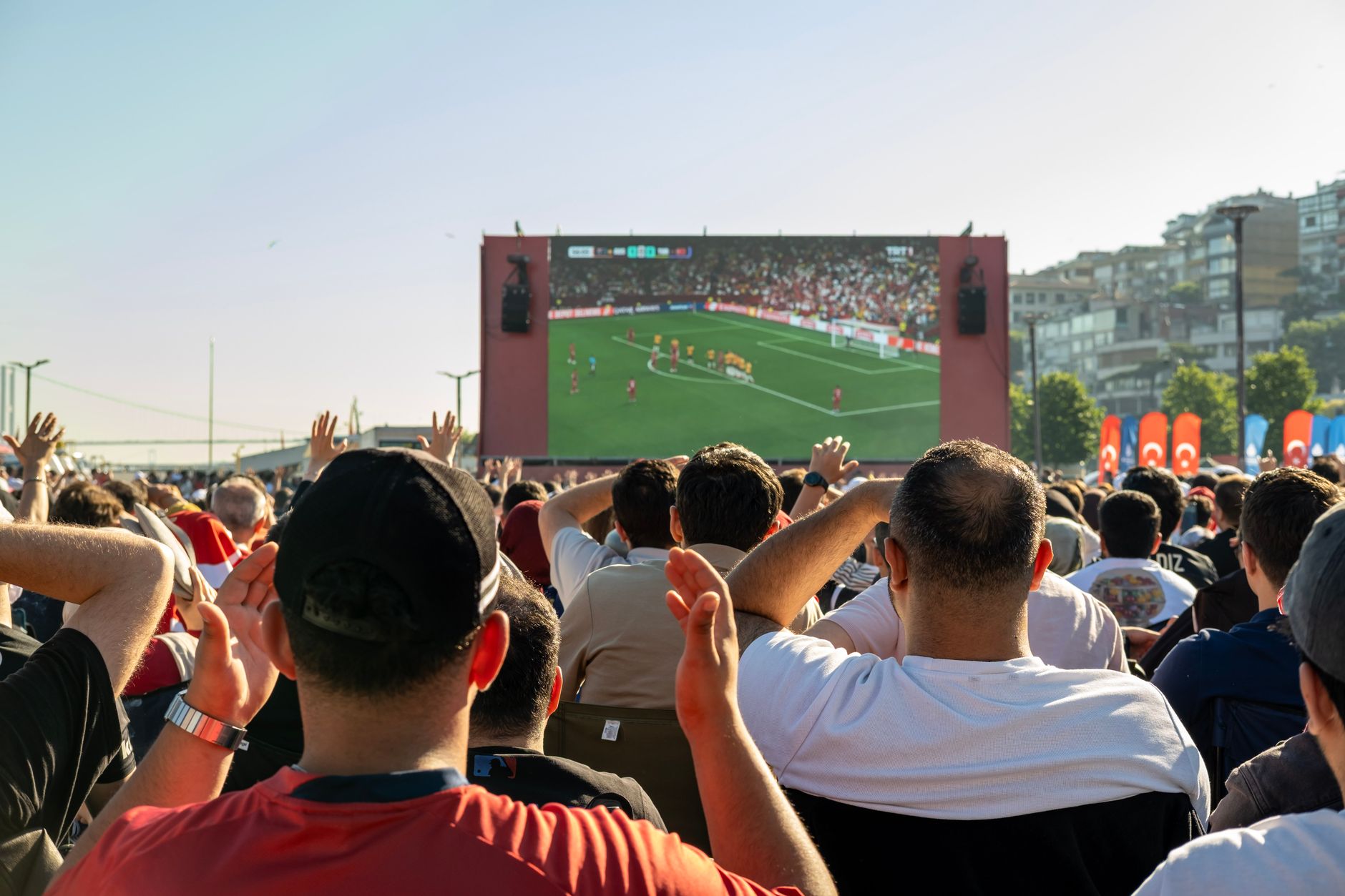 Kerumunan menonton pertandingan sepak bola di layar besar di luar ruangan di Istanbul, Türkiye.