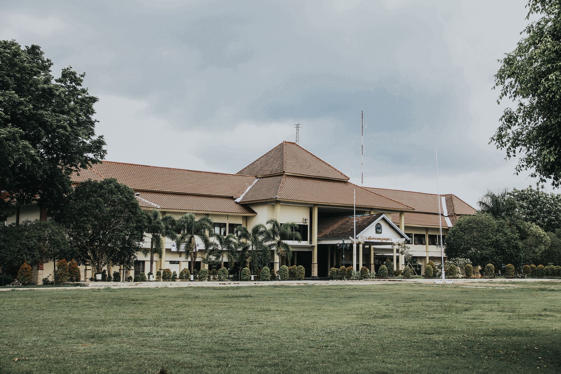 Bangunan bergaya kolonial di Yogyakarta, Indonesia, dikelilingi oleh pepohonan hijau dan pohon palem.