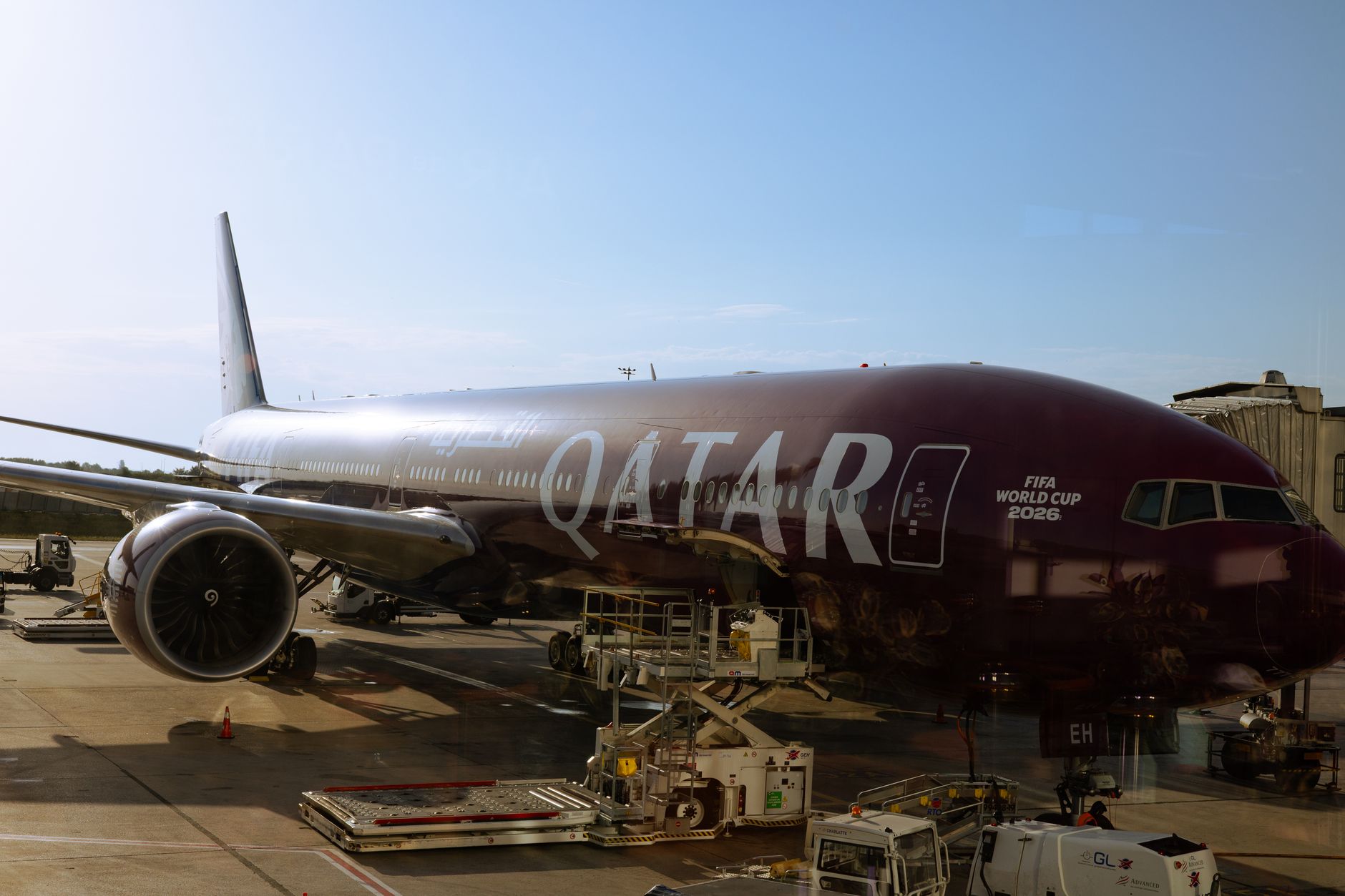 Pesawat Qatar Airways dengan branding Piala Dunia FIFA 2026 di terminal bandara di bawah langit jernih.