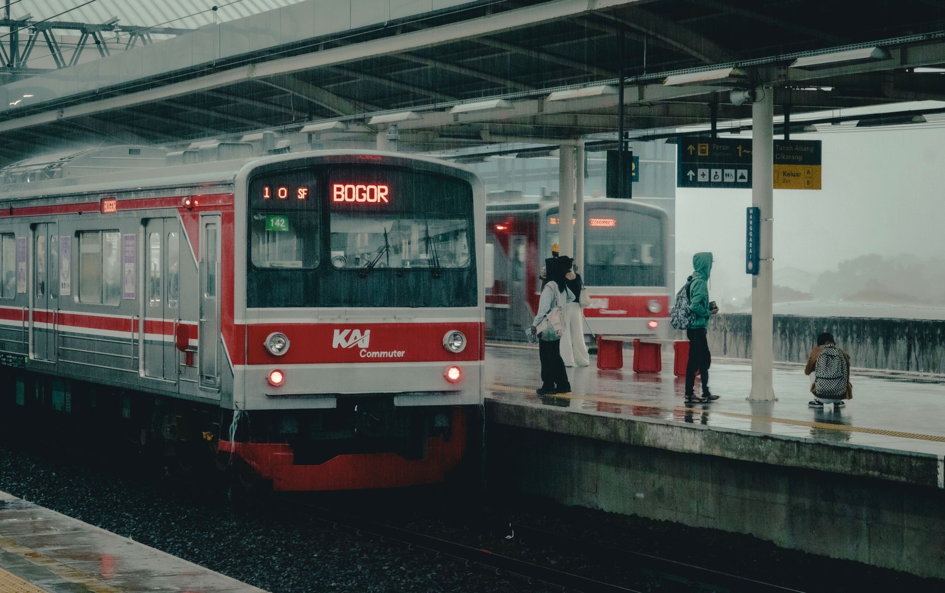 Para penumpang di stasiun Bogor menaiki kereta api pada hari hujan, Indonesia.