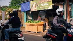 Pasar jalanan yang ramai di Jawa Barat dengan orang-orang yang mengendarai sepeda motor melewati kios alpukat.