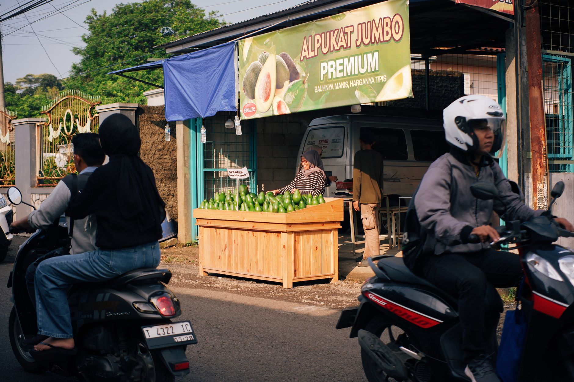 Pasar jalanan yang ramai di Jawa Barat dengan orang-orang yang mengendarai sepeda motor melewati kios alpukat.