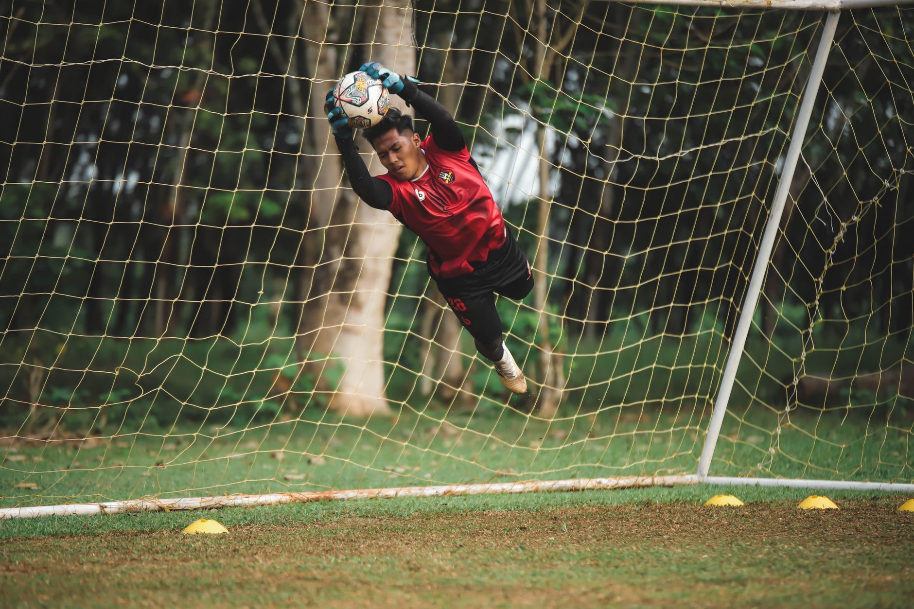 Kiper sepak bola yang melakukan tangkapan mengesankan di udara selama pertandingan di lapangan hijau.