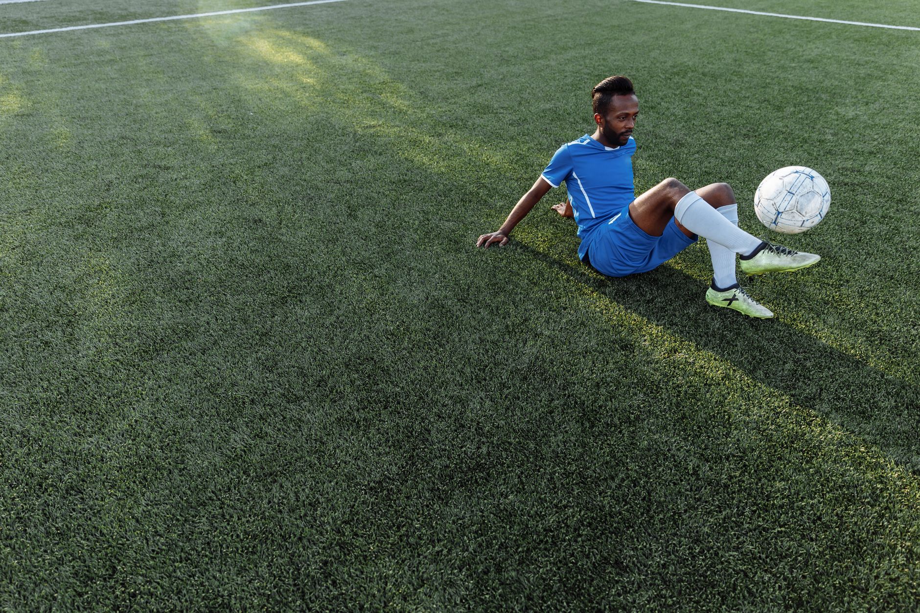 Seorang atlet melatih kemampuan sepak bola di lapangan rumput di bawah sinar matahari.