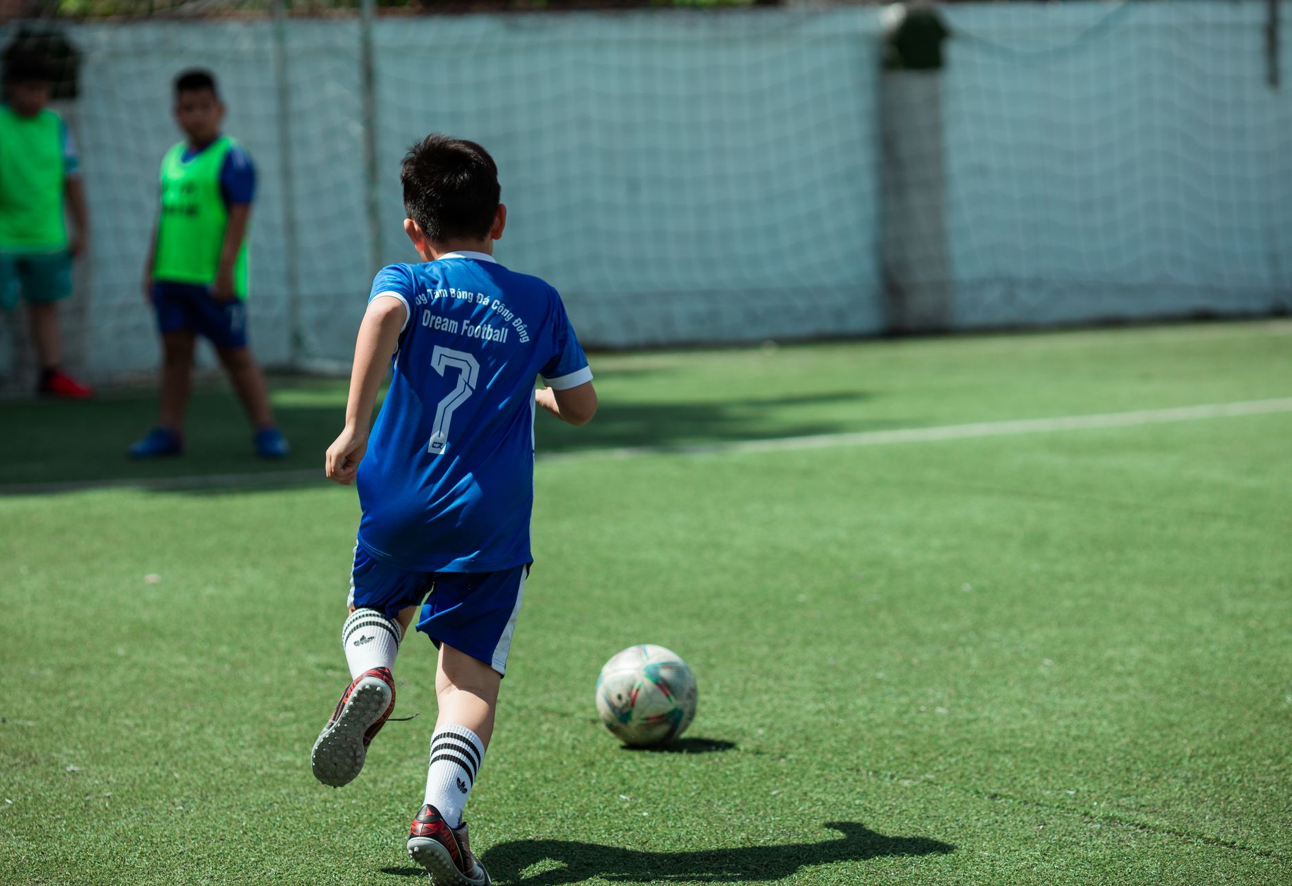 Seorang anak laki-laki bermain sepak bola di lapangan yang cerah, menunjukkan sportivitas dan kesenangan. Ideal untuk konten yang berkaitan dengan olahraga.