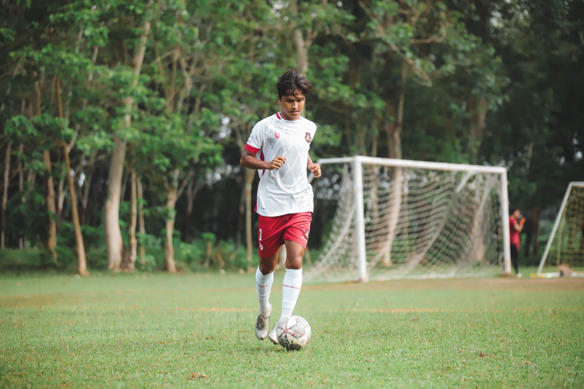 Pemain sepak bola remaja menggiring bola di lapangan sepak bola yang hijau subur.