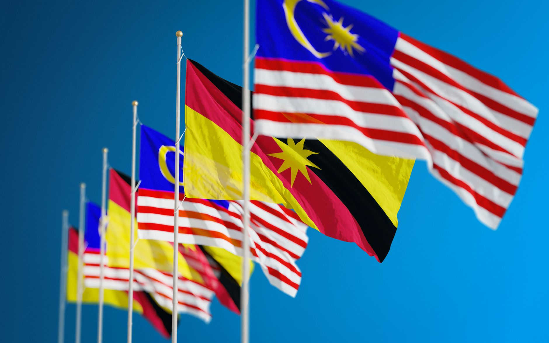 Pertunjukan cerah dari bendera Malaysia dan Sarawak yang melambangkan persatuan dan patriotisme di balik langit biru yang cerah.