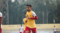 Pengambilan gambar dinamis seorang pemain sepak bola di tengah permainan di lapangan terbuka, menunjukkan tekad dan fokus.