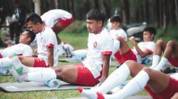 Pemain sepak bola dalam sesi latihan melakukan peregangan di lapangan di Jakarta.