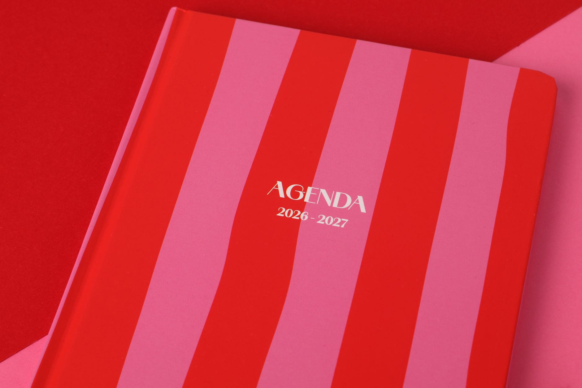 Buku agenda bergaris merah dan merah muda untuk tahun 2026-2027, sempurna untuk perencanaan.