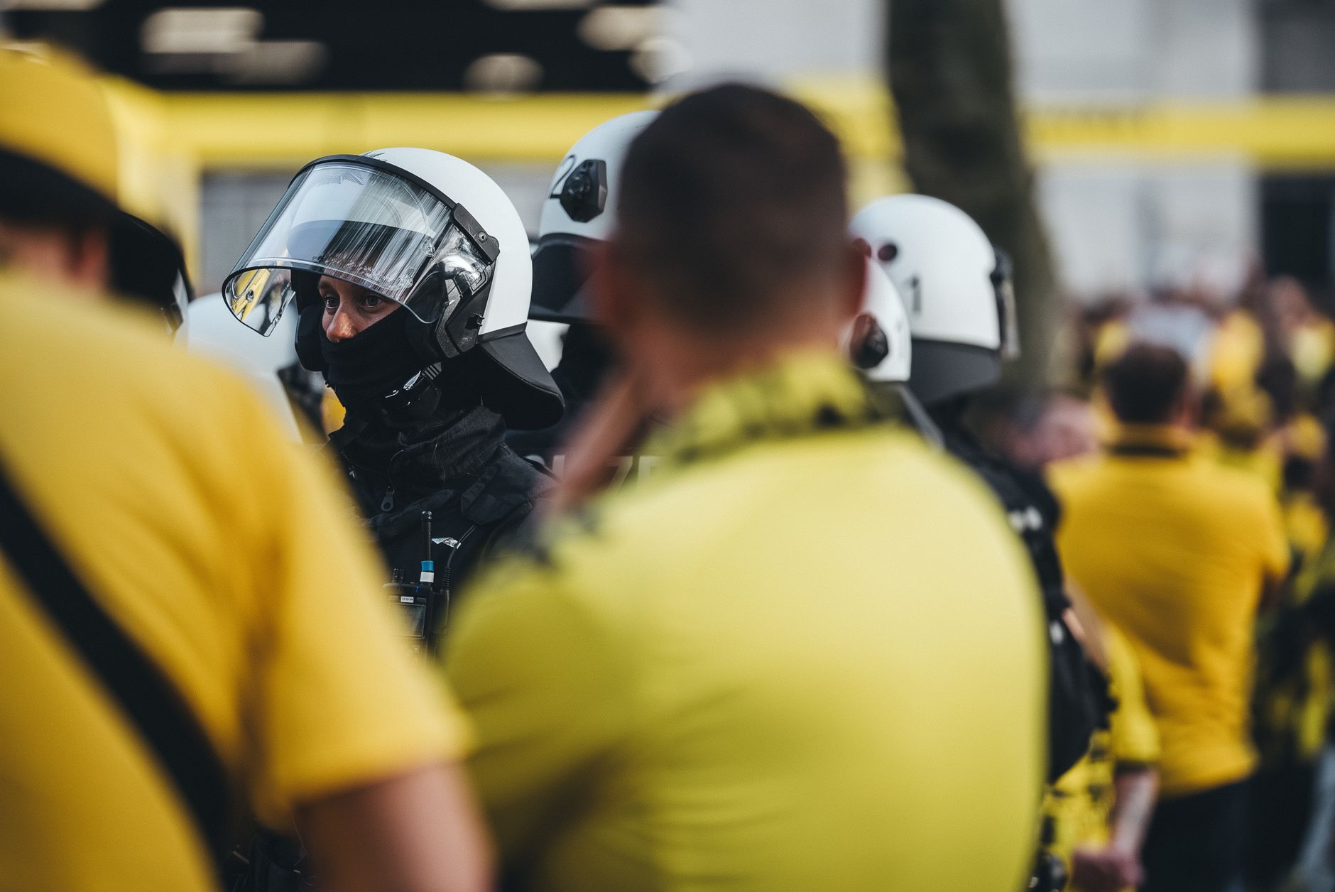 Petugas polisi dengan perlengkapan pelindung selama demonstrasi publik dengan kerumunan di latar belakang.