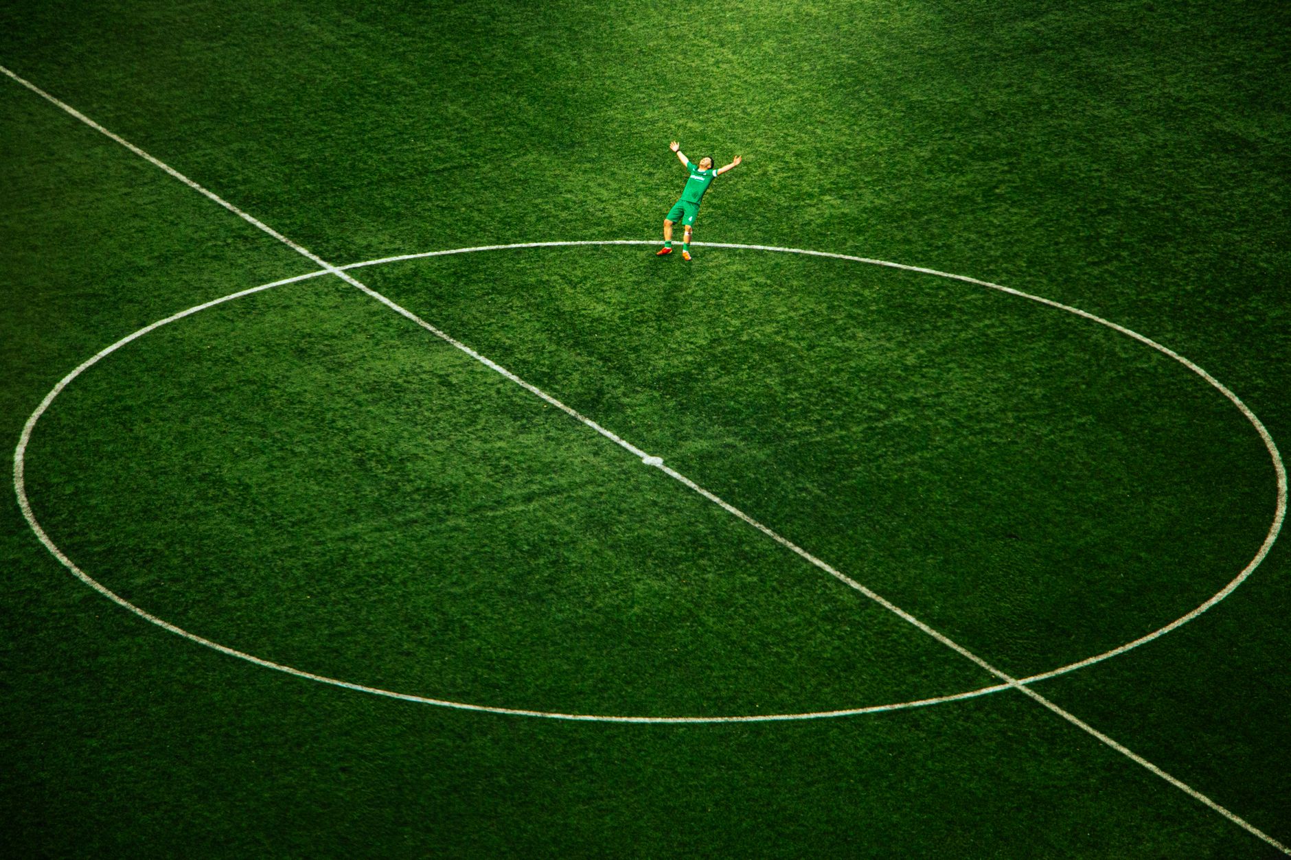 Seorang pemain sepak bola merayakan golnya di lapangan kosong, disorot lampu di lingkaran tengah stadion.