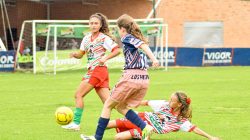 Gadis yang terlibat dalam pertandingan sepak bola yang kompetitif, menampilkan aksi olahraga yang dinamis di lapangan hijau yang cerah.