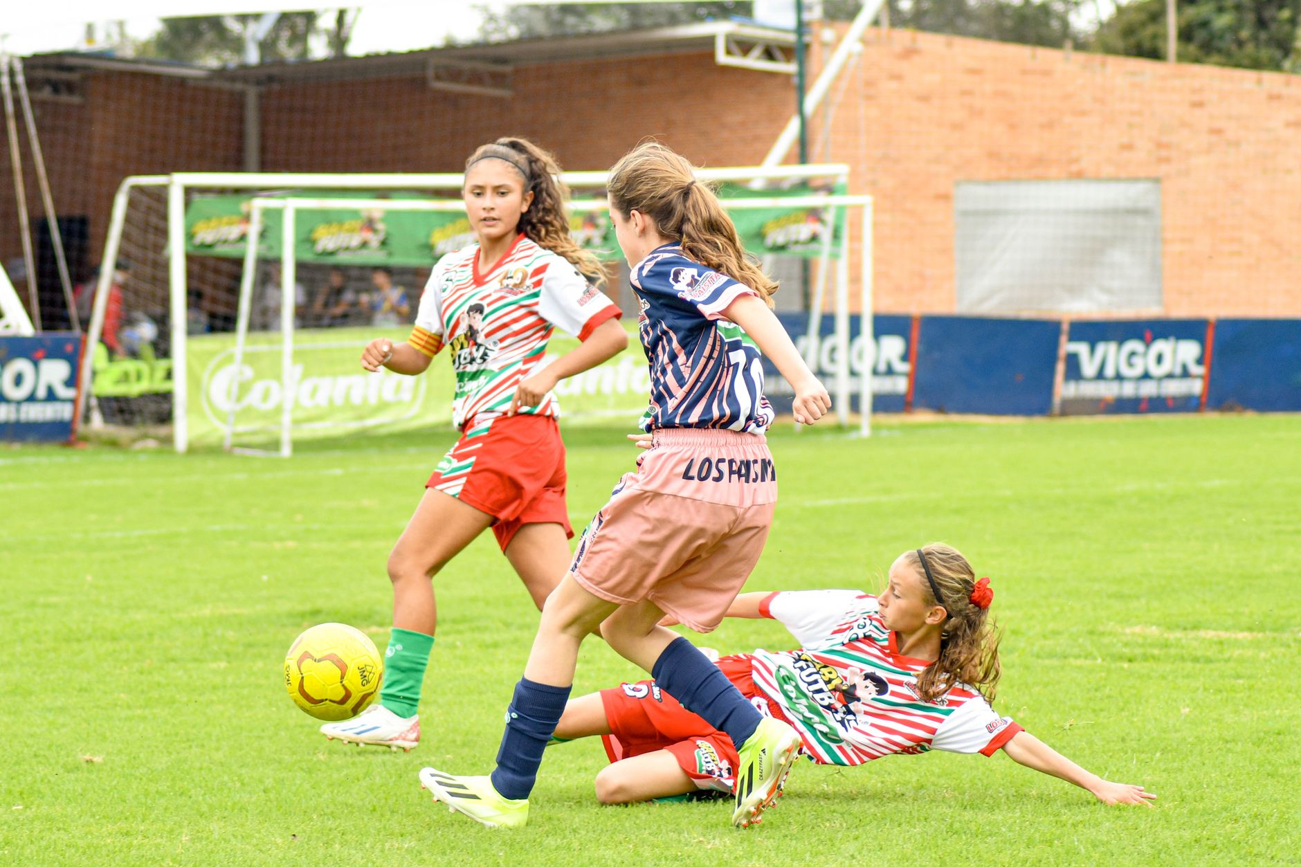 Gadis yang terlibat dalam pertandingan sepak bola yang kompetitif, menampilkan aksi olahraga yang dinamis di lapangan hijau yang cerah.