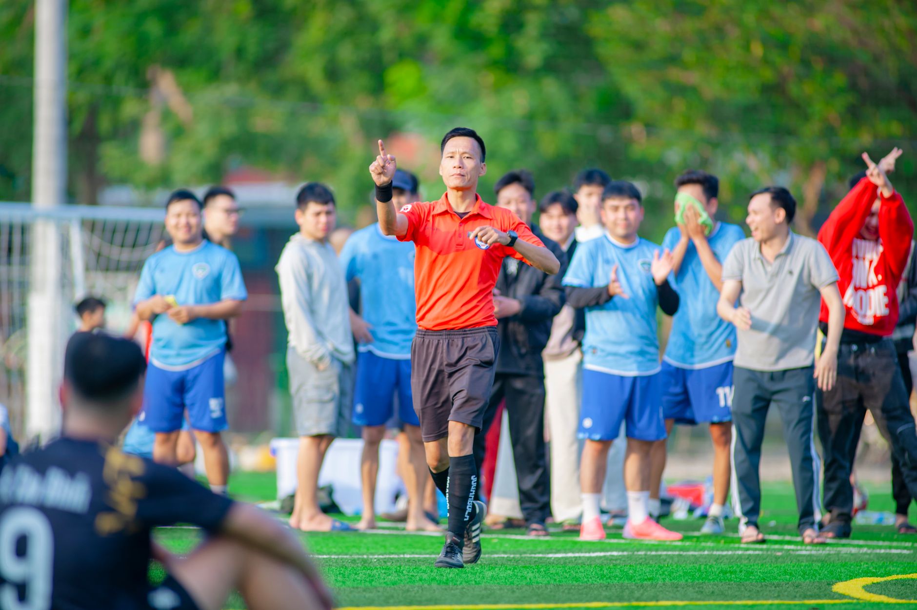Wasit memberikan sinyal selama pertandingan sepak bola di Hà Nội dengan pemain dan penonton di latar belakang.