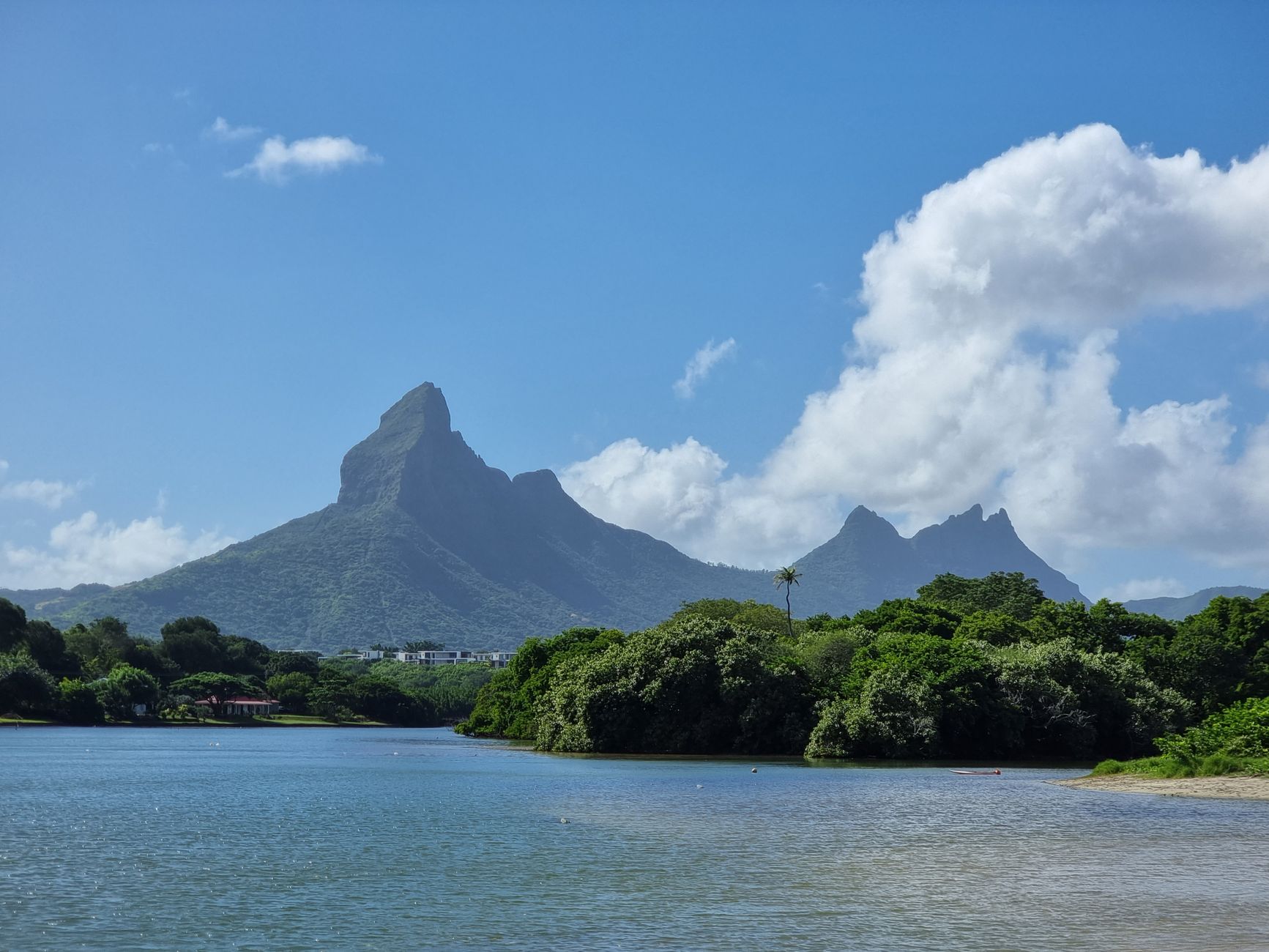 Gambar gunung dan lagun ikonik Mauritius di bawah langit biru yang cerah.