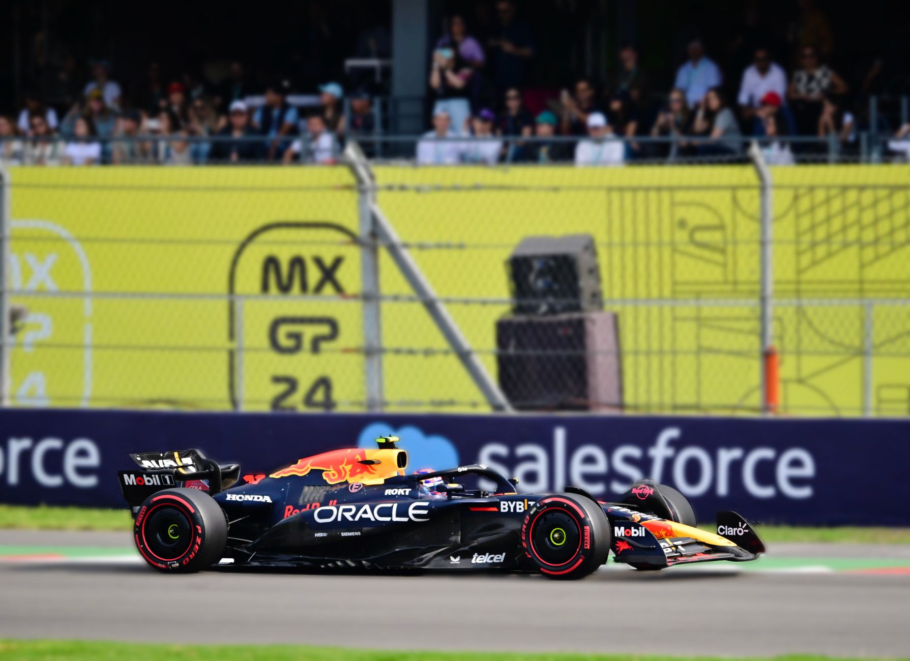 Bidikan dinamis dari mobil F1 yang balapan di Grand Prix Kota Meksiko dengan kerumunan yang bersorak di latar belakang.