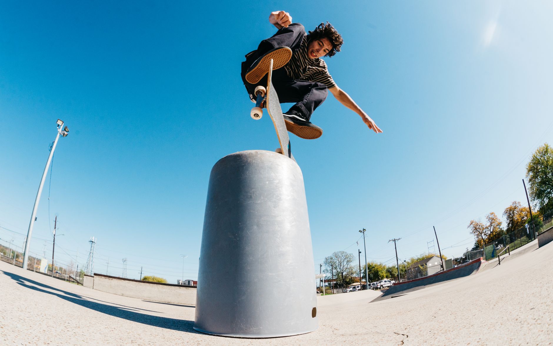 Pemain skateboard yang melakukan trik di taman skateboard luar ruangan yang cerah.