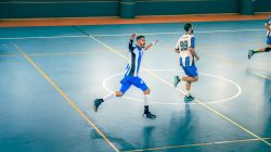 Pertandingan futsal dalam ruangan yang penuh aksi dengan pemain bergerak di lapangan.