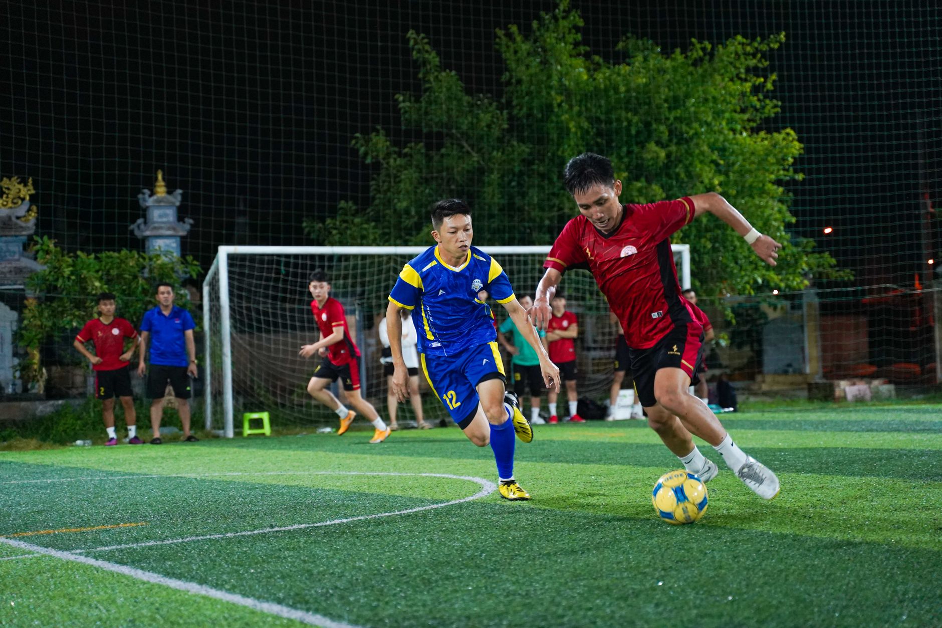 Cetak gambar dinamis pemain sepak bola yang bersaing dalam pertandingan malam di lapangan rumput.