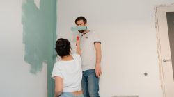 Sepasang kekasih berkolaborasi untuk mengecat ruangan dengan warna cerah, fokus pada kerja sama dan perbaikan rumah.