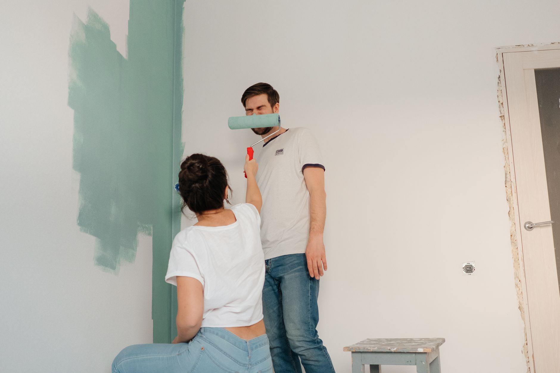 Sepasang kekasih berkolaborasi untuk mengecat ruangan dengan warna cerah, fokus pada kerja sama dan perbaikan rumah.
