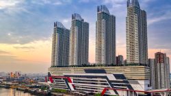 Pemandangan udara gedung pencakar langit modern di Jakarta, Indonesia, saat matahari terbit yang tercermin di air.