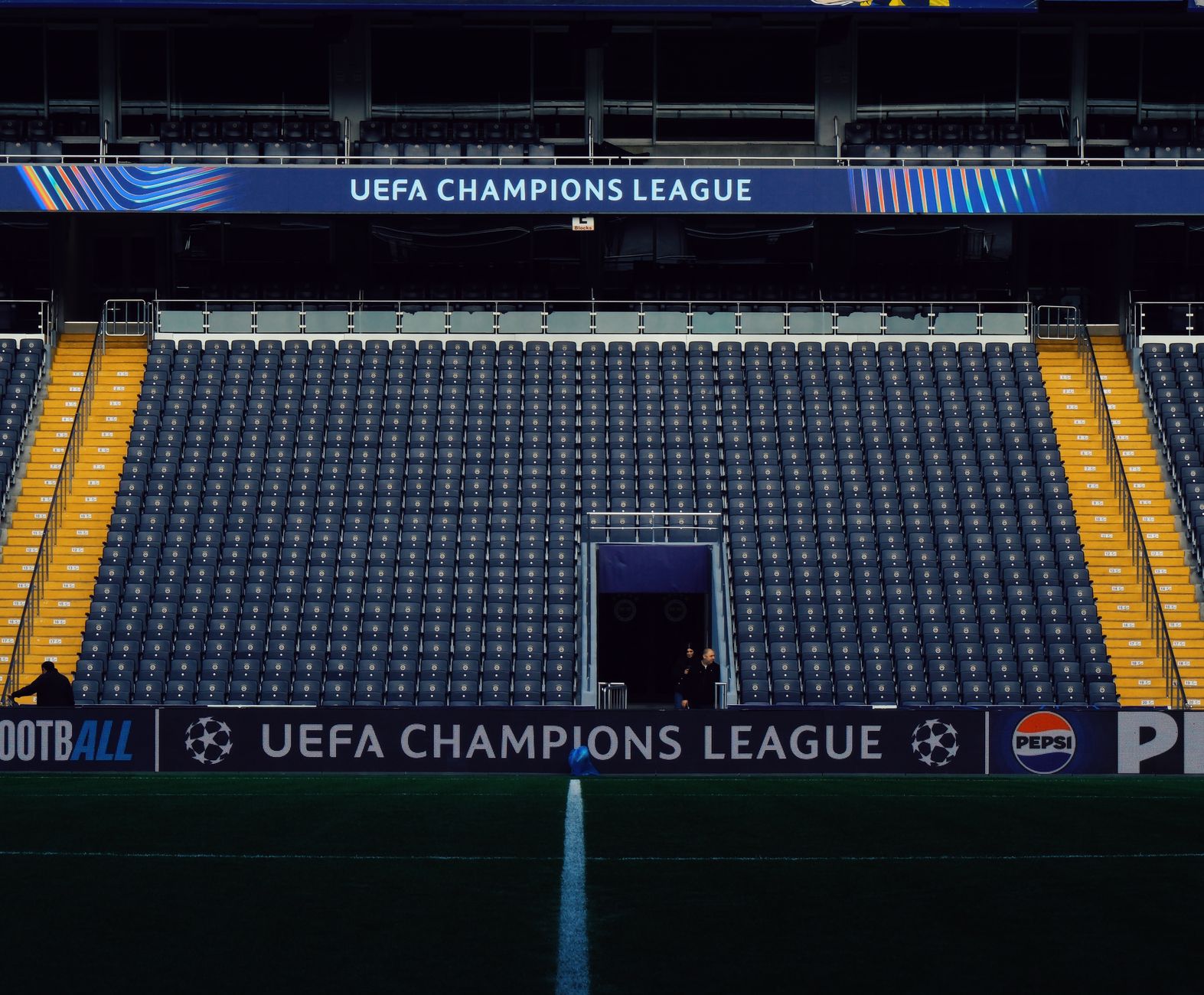 Kursi stadion kosong dengan papan nama UEFA Champions League dan penonton yang minim.