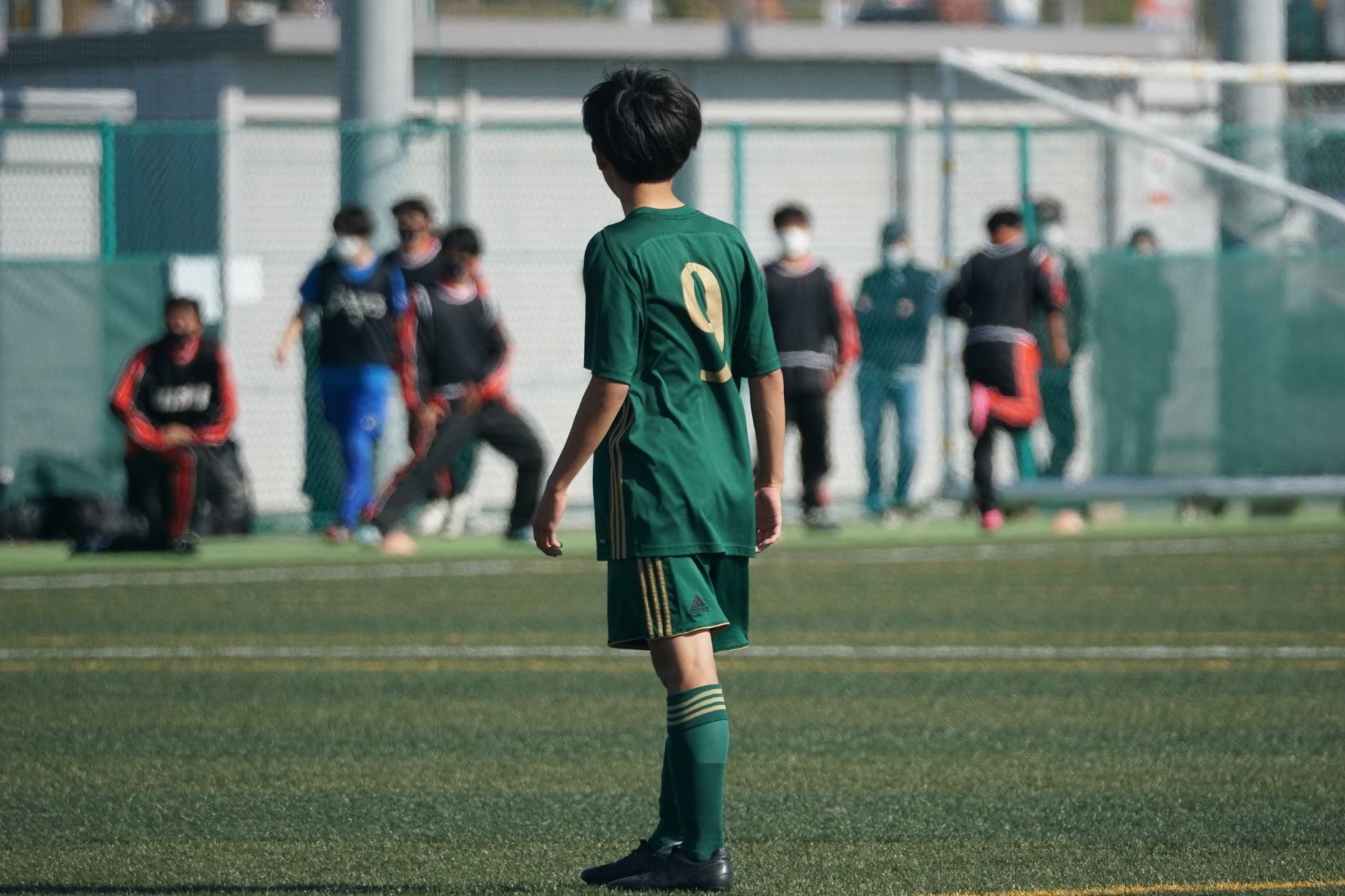 Pemain sepak bola muda dengan jersey hijau di lapangan sepak bola saat pertandingan.